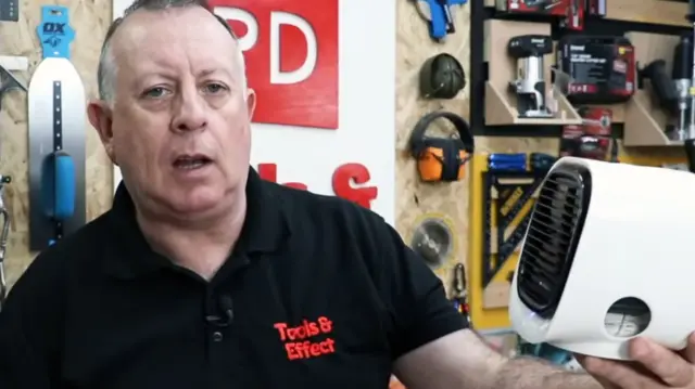 Stuart Matthews in a grab from his You Tube channel Proper DIY in a black t shirt holding the white cube fan